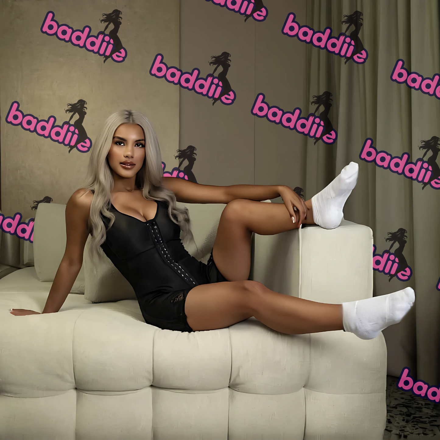 Woman sitting on a couch wearing black shapewear with 'baddiie' branding in the background.